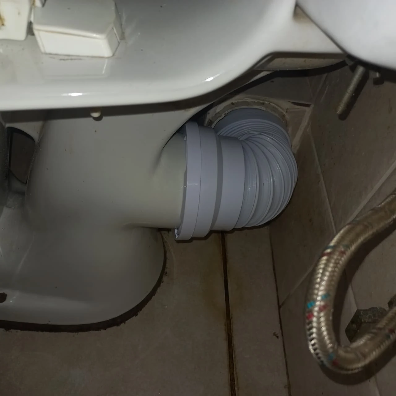 Flexible pan connector fitted behind a toilet during blocked-toilet repair work.