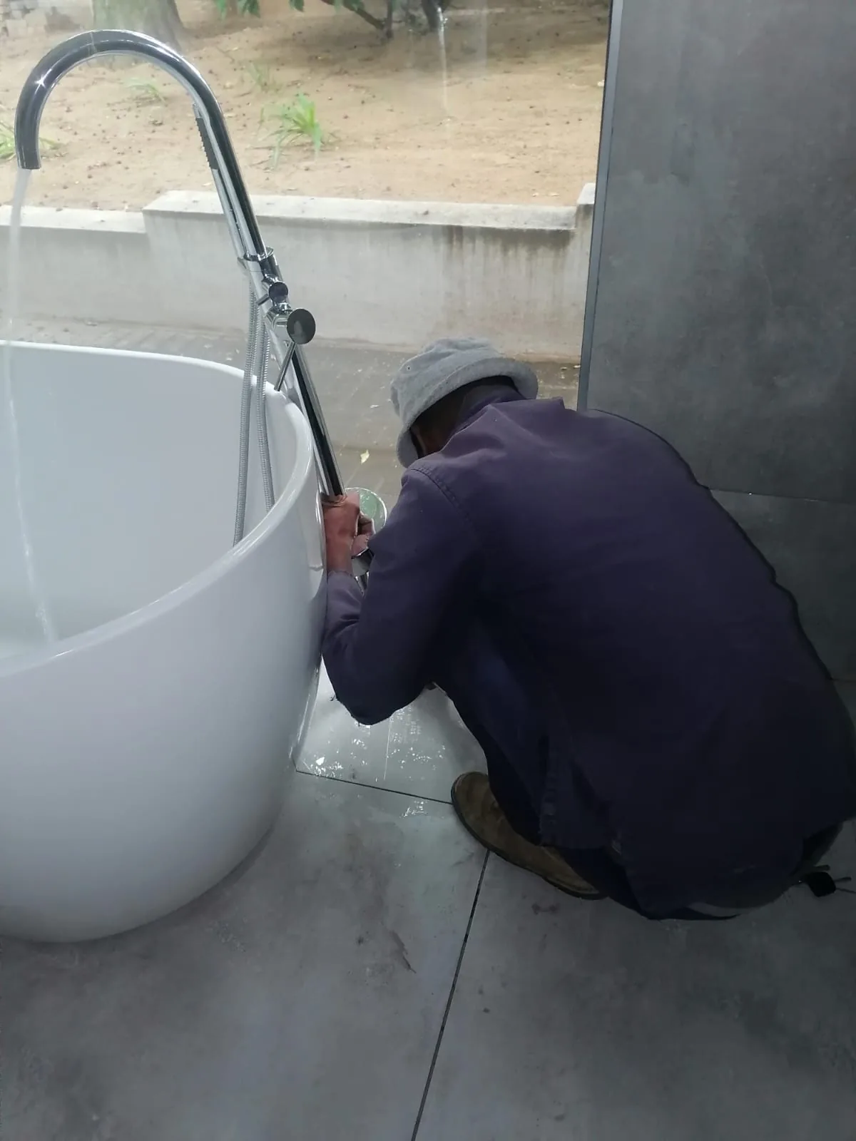 Technician working beside a freestanding bath tap during a Bordeaux bathroom plumbing repair.