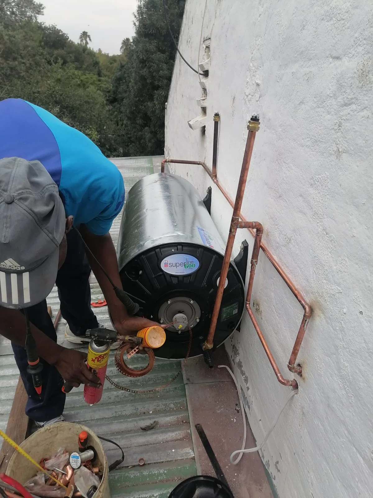Geyser maintenance with copper pipework and technician working on a roof installation.