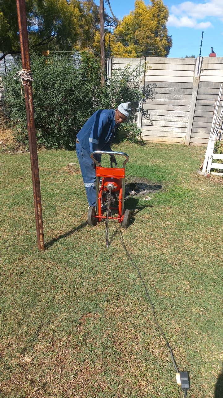 Randburg plumber clearing a drain with professional drain equipment on a lawn.